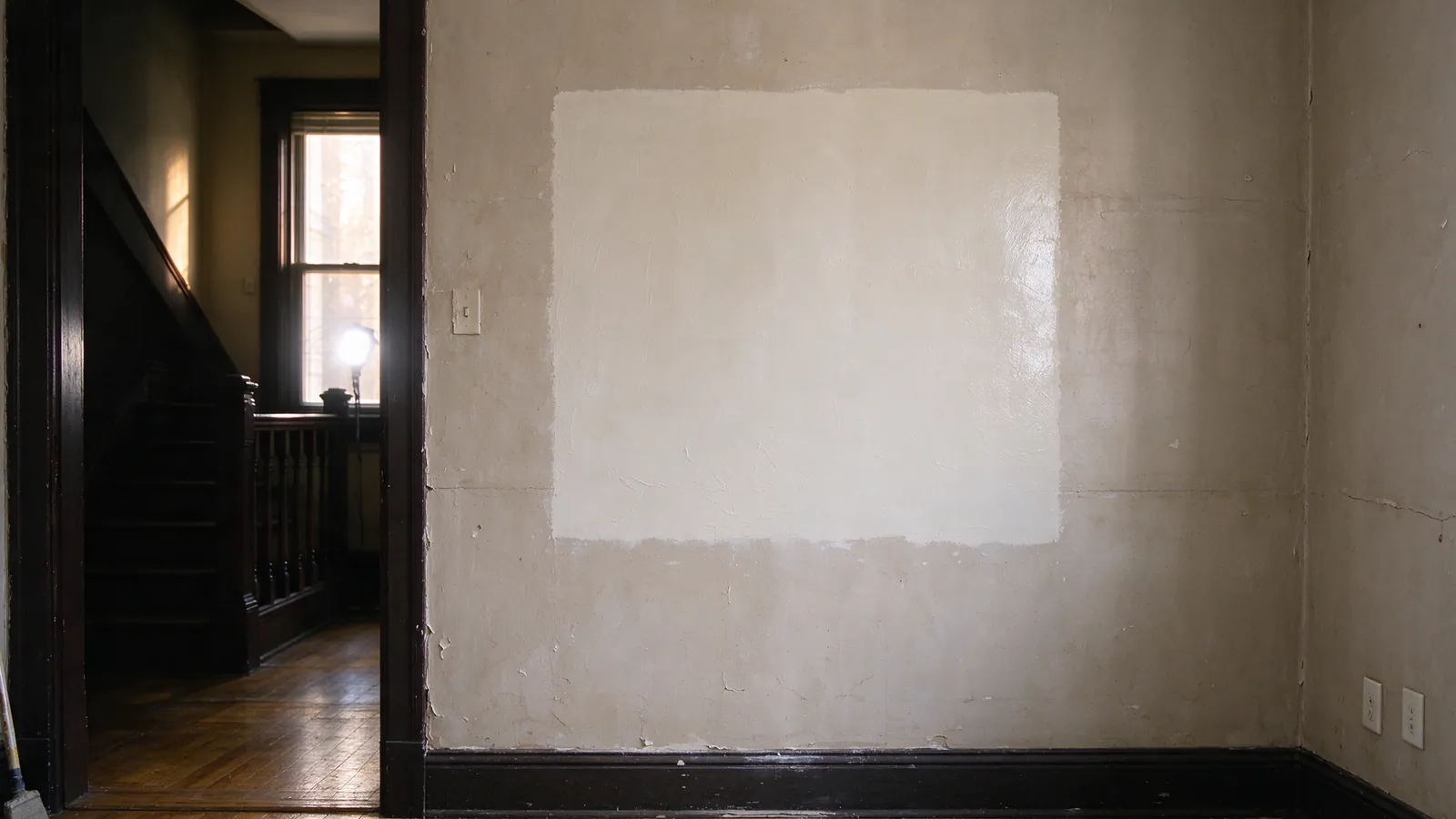 A neat rectangular opening cut in an old plaster and wood lath wall, showing new red and blue PEX lines rising behind it, with plastic sheeting taped around the work area