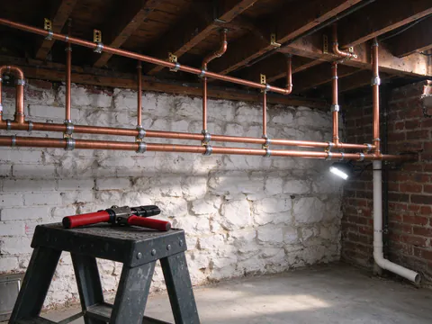 New copper water lines with press fittings running along the ceiling of a corner-store basement in Philadelphia, strapped to the joists with copper hangers