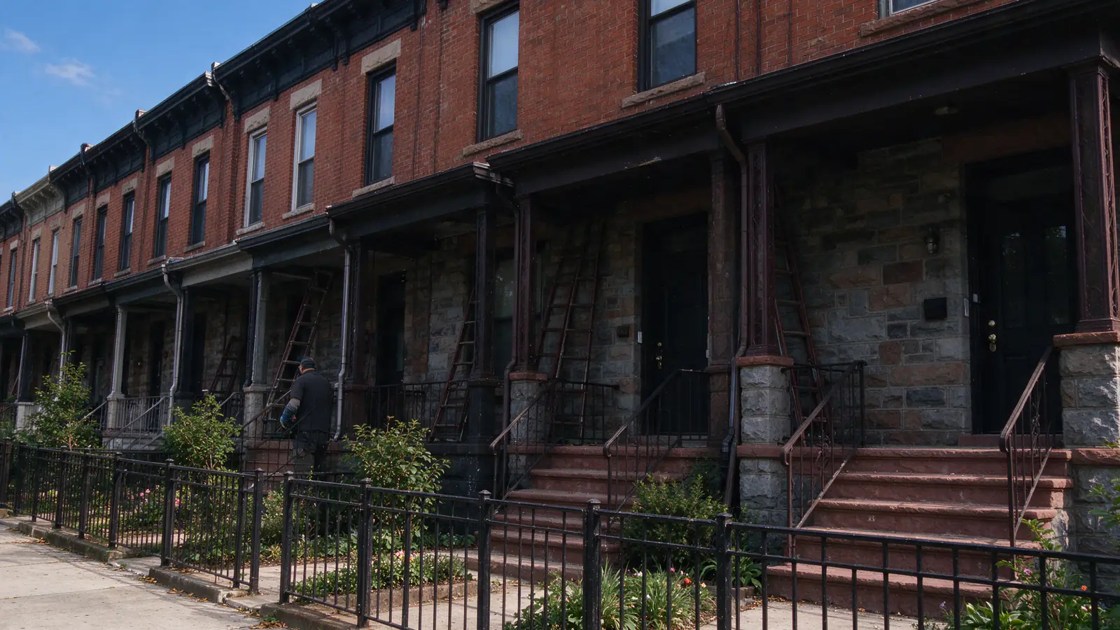 A home buyer and an inspector with a flashlight looking at an old water meter and a gray service pipe entering through the stone front wall of a rowhouse basement